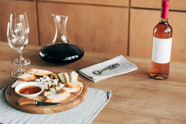 Botella de vino, jarra, copas de vino y comida en la mesa de madera - foto de stock