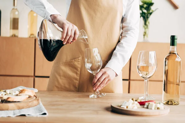 Visão parcial de sommelier em avental segurando jarro e derramando vinho em copo de vinho — Fotografia de Stock