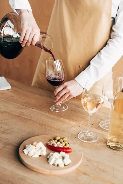 Vista parziale del sommelier in brocca di azienda grembiule e versando vino in bicchiere di vino — Foto stock