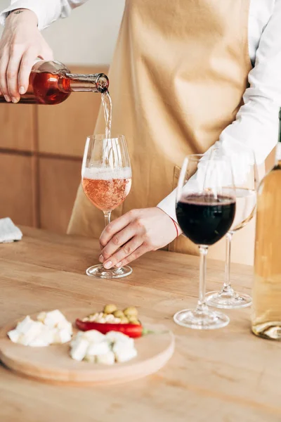 Partial view of sommelier in apron holding bottle and pouring wine in wine glass — Stock Photo