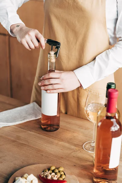 Vista parziale del sommelier in grembiule aprendo bottiglia di vino — Foto stock