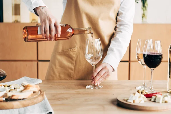 Vue partielle du sommelier dans le tablier tenant la bouteille et versant le vin dans le verre à vin — Photo de stock