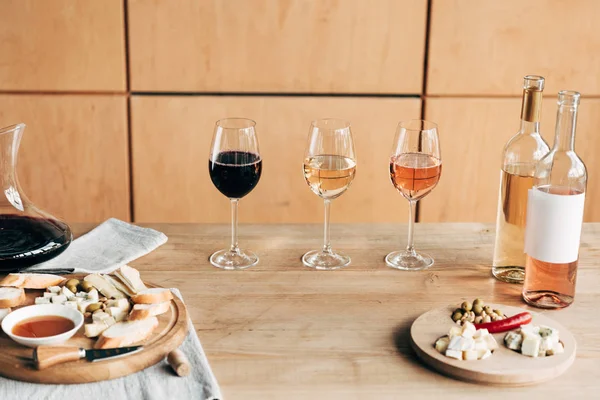 Copas de vino, botellas de vino y comida en mesa de madera - foto de stock