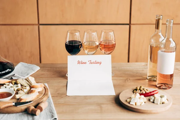 Copas de vino, botellas, documento de degustación de vinos y comida en mesa de madera - foto de stock