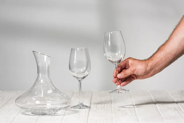 Cropped view of man holding empty wine glass above wooden surface in restaurant — Stock Photo