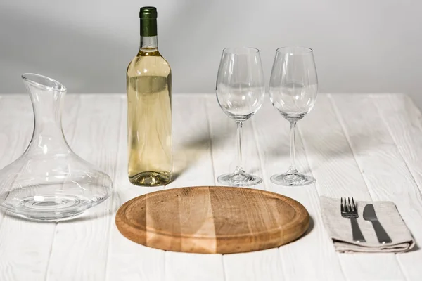 Botella de vino, jarra, copas de vino, cubiertos y tabla de cortar en la superficie de madera en el restaurante - foto de stock