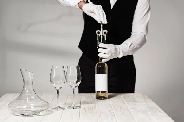 Partial view of waiter in white gloves opening bottle of wine with corkscrew — Stock Photo