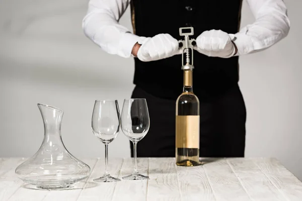 Vista parcial del camarero en guantes blancos abriendo botella de vino con sacacorchos - foto de stock