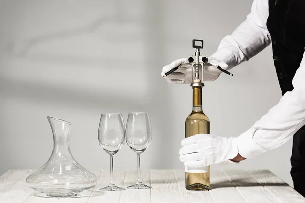 Vista parziale del cameriere in guanti bianchi aprendo bottiglia di vino con cavatappi nel ristorante — Foto stock