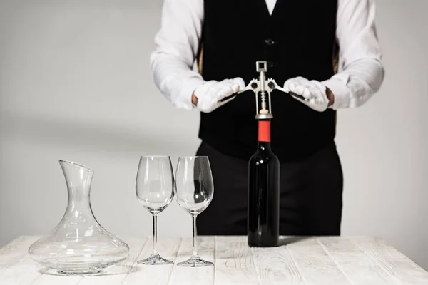 Partial view of waiter in white gloves opening bottle of wine with corkscrew in restaurant — Stock Photo