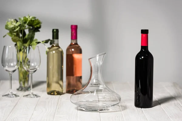 Bottles of wine, wine glases, vase with green plants and jug on wooden surface — Stock Photo