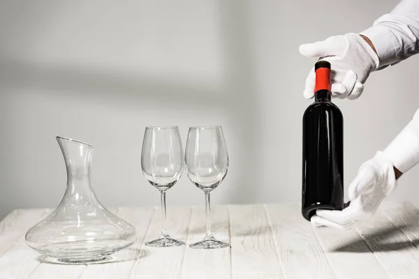 Cropped view of waiter in white gloves holding bottle of wine — Stock Photo