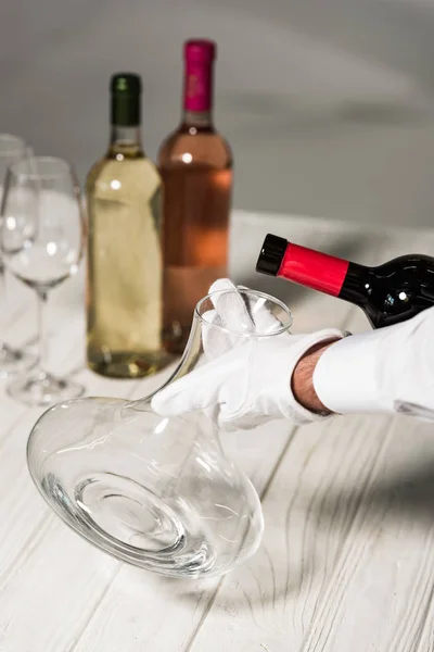 Vue partielle du serveur en gant blanc versant du vin dans une cruche — Photo de stock