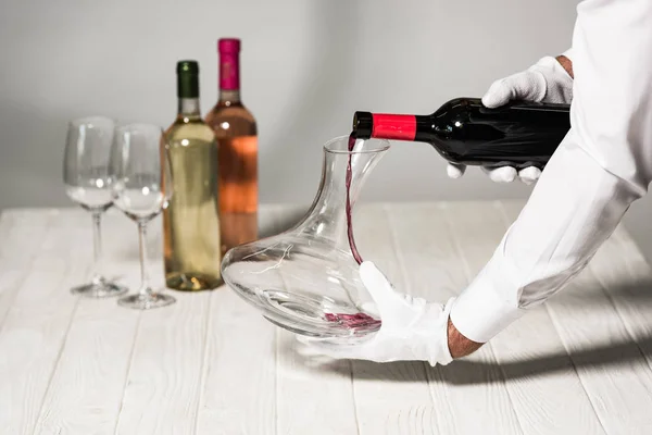 Vue partielle du serveur en gants blancs versant du vin dans une cruche — Photo de stock