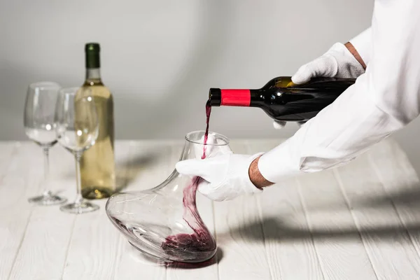 Vue partielle du serveur en gants blancs versant du vin dans une cruche — Photo de stock