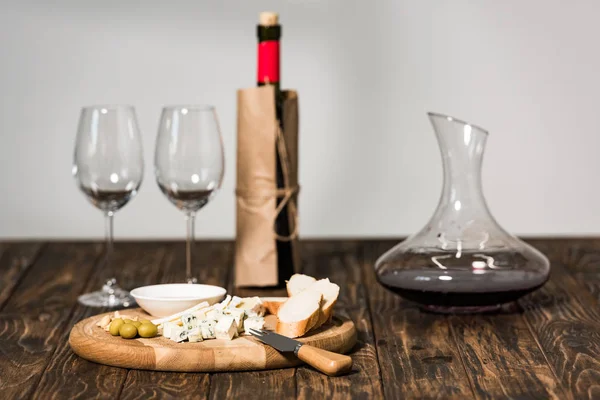 Botella de vino, copas de vino, jarra, queso, aceitunas y pan en la superficie de madera - foto de stock