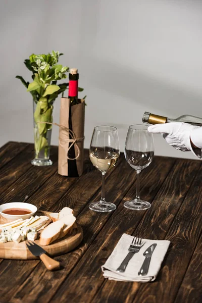 Partial view of waiter in white glove pouring wine in wine glasses in restaurant — Stock Photo