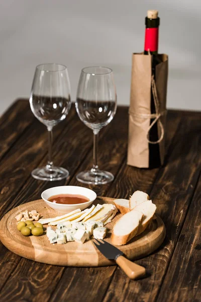 Bottiglia di vino, bicchieri di vino, formaggio, olive, salsa e pane su superficie di legno — Foto stock