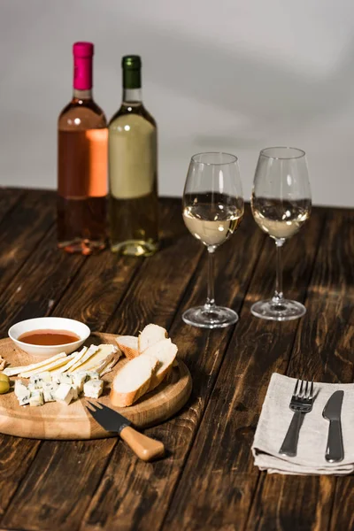Bottiglie di vino, bicchieri di vino, posate, formaggio, olive, salsa e pane su superficie di legno — Foto stock