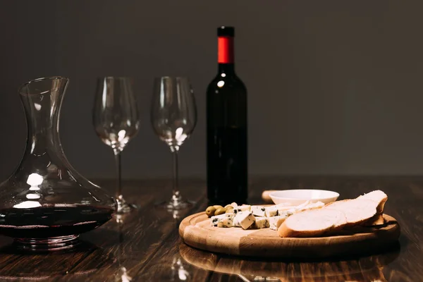 Cheese, bread, sauce, bottle of wine, wine glasses and jug on wooden surface — Stock Photo