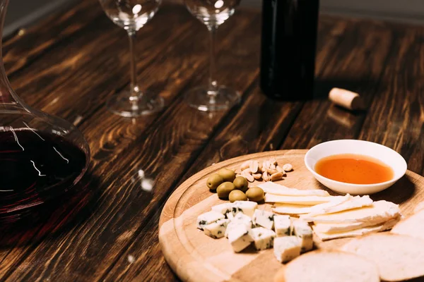 Cheese, bread, sauce, bottle of wine, wine glasses and jug on wooden surface — Stock Photo