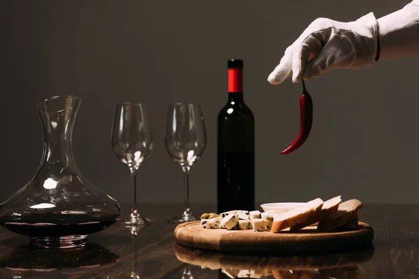 Vista recortada del camarero en guante blanco sosteniendo pimienta cerca de la mesa con comida y vino - foto de stock
