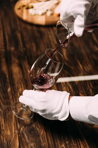 Vista cortada de garçom em luvas brancas derramando vinho em copo de vinho — Fotografia de Stock