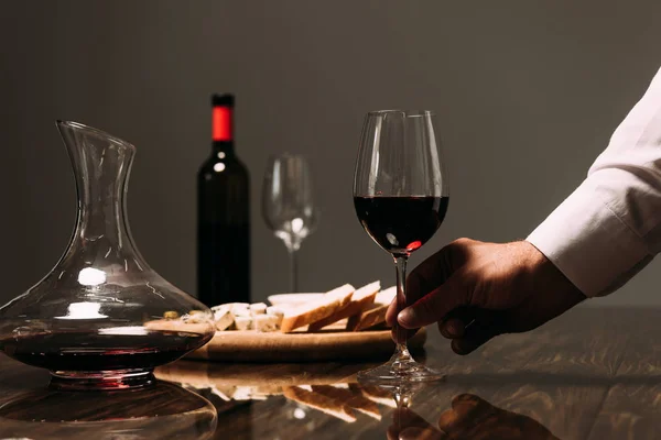 Vista recortada del hombre sosteniendo copa de vino en la mesa en el restaurante - foto de stock