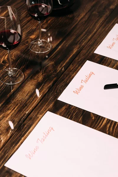 Documentos de cata de vinos, bolígrafos y copas de vino sobre mesa de madera - foto de stock