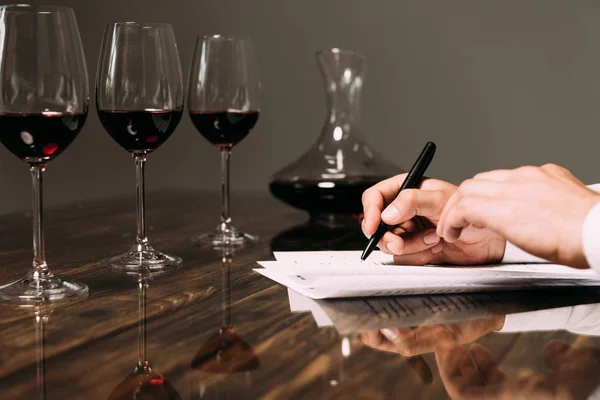 Частичный вид сомелье, пишущего за столом с бокалами для вина — стоковое фото