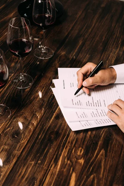 Vue partielle du sommelier écrivant à table avec des verres à vin — Photo de stock