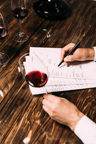 Ausgeschnittene Ansicht eines Sommeliers, der Dokumente am Tisch aufschreibt und ein Weinglas hält — Stockfoto