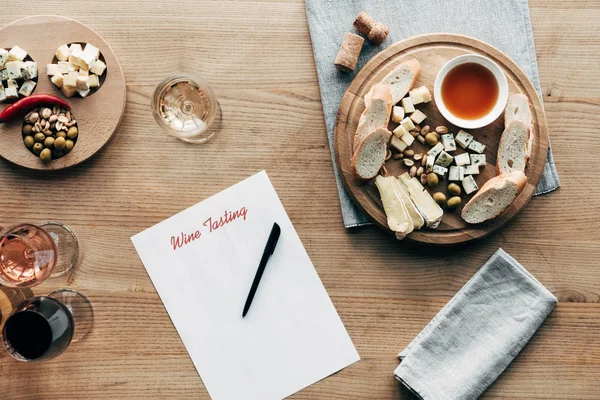 Top view of wine tasting document, pen, wine glasses, food and corks on wooden surface — Stock Photo