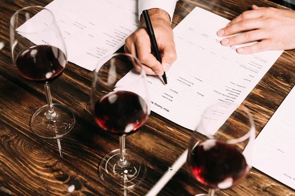 Cropped view of sommelier writing in documents at table with wine glasses — Stock Photo
