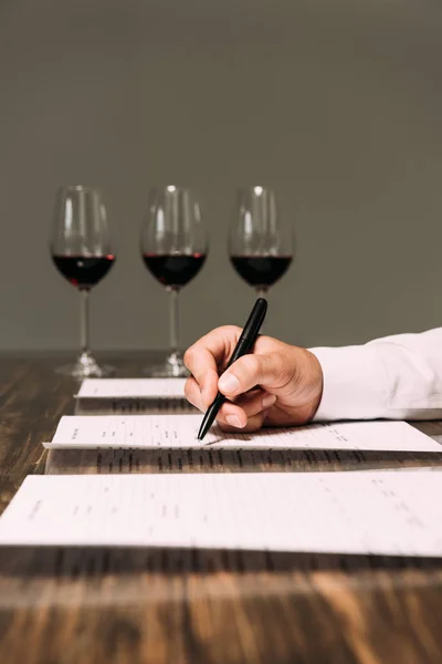 Cropped view of sommelier writing in documents at table with wine glasses — Stock Photo