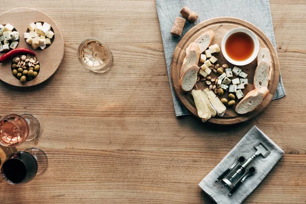 Top view of wine glasses, food, corkscrew and corks on wooden surface — Stock Photo