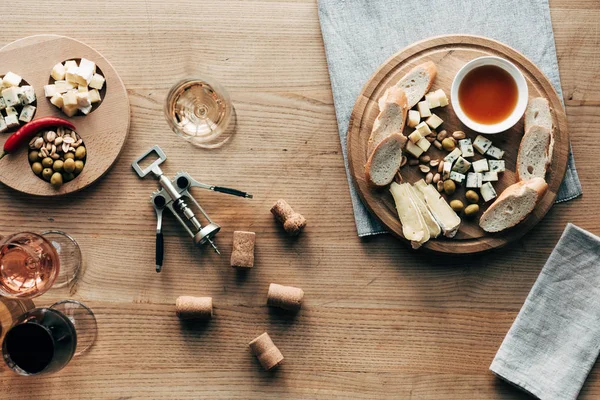 Draufsicht auf Weingläser, Lebensmittel, Korkenzieher und Korken auf Holzoberfläche — Stockfoto