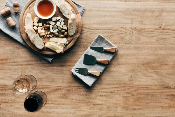 Vue de dessus des verres à vin, sauce, pain, fromage, olives, bouchons et ustensiles de cuisine sur la surface en bois — Photo de stock