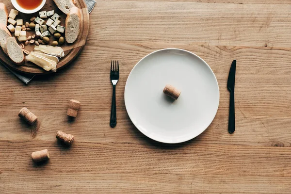 Top view of plate with cork, cutlery and food on wooden table — Stock Photo