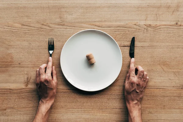 Vista cortada do homem segurando garfo e faca à mesa com placa e cortiça — Fotografia de Stock