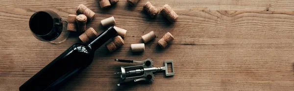 Panoramic shot of bottle of wine, wine glass, corkscrew and corks on wooden surface — Stock Photo