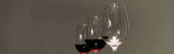 Tiro panorâmico de três copos de vinho com vinho tinto isolado em cinza — Fotografia de Stock