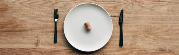 Panoramic shot of plate with cork and cutlery on wooden surface — Stock Photo