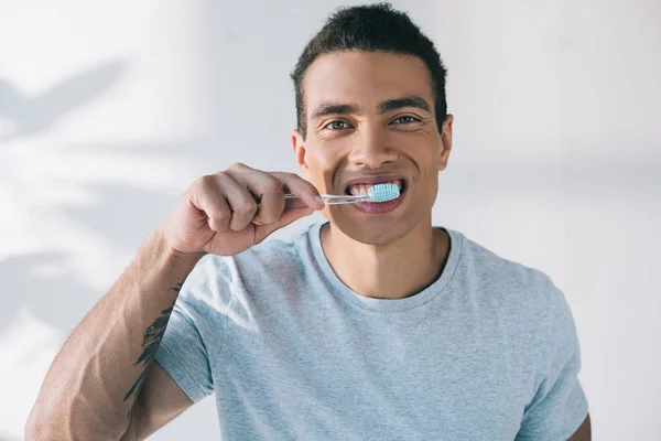 Junger Mann putzt Zähne mit Zahnbürste und blickt in Kamera — Stockfoto
