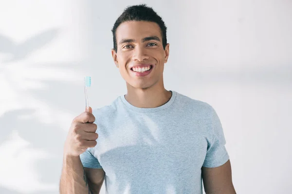 Schöner junger Mann mit Zahnbürste, lächelt und blickt in die Kamera — Stockfoto
