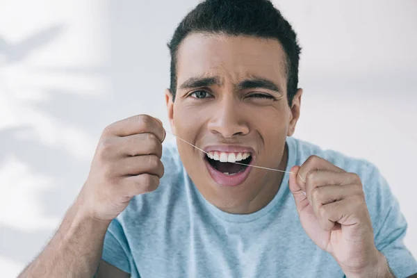 Junger Mann, der Schmerzen verspürt, während er Zahnseide benutzt und in die Kamera schaut — Stockfoto