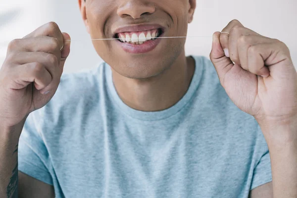 Обрезанный вид молодого человека, улыбающегося и пользующегося зубной нитью — стоковое фото