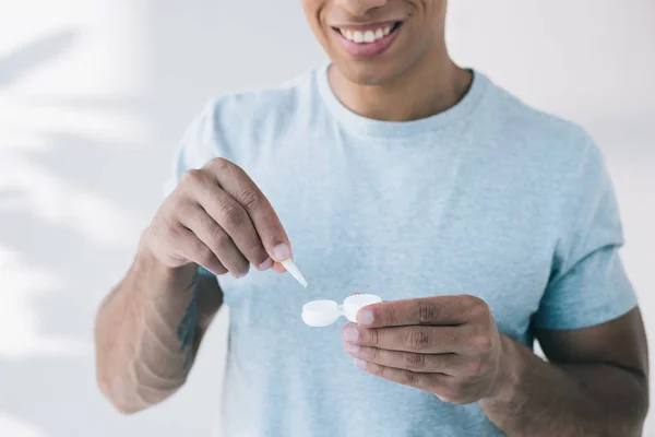 Vue recadrée de l'homme tenant le récipient et prenant la lentille de contact avec une pince à épiler — Photo de stock