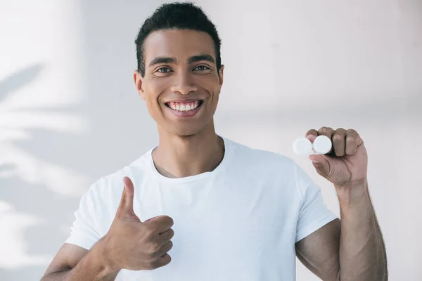 Handsome young man holding container for contact lens and showing thumb up — Stock Photo