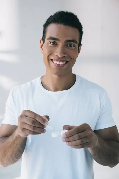 Young man smiling and looking at camera while putting lens solution into container with lens — Stock Photo